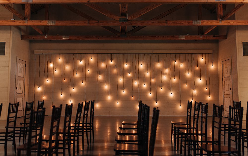 hanging twinkle lights on the wall of indoor ceremony space at The Barn at Shady Lane wedding venue