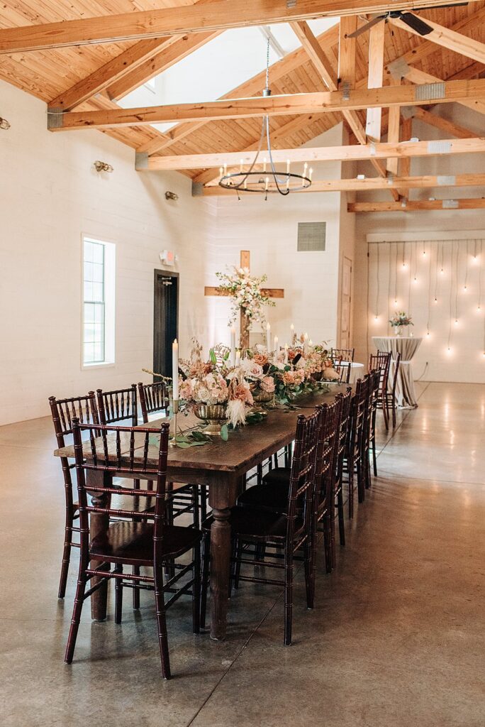 long farm wood tables under wooden beams and candelabras at The Barn at Shady Lane venue
